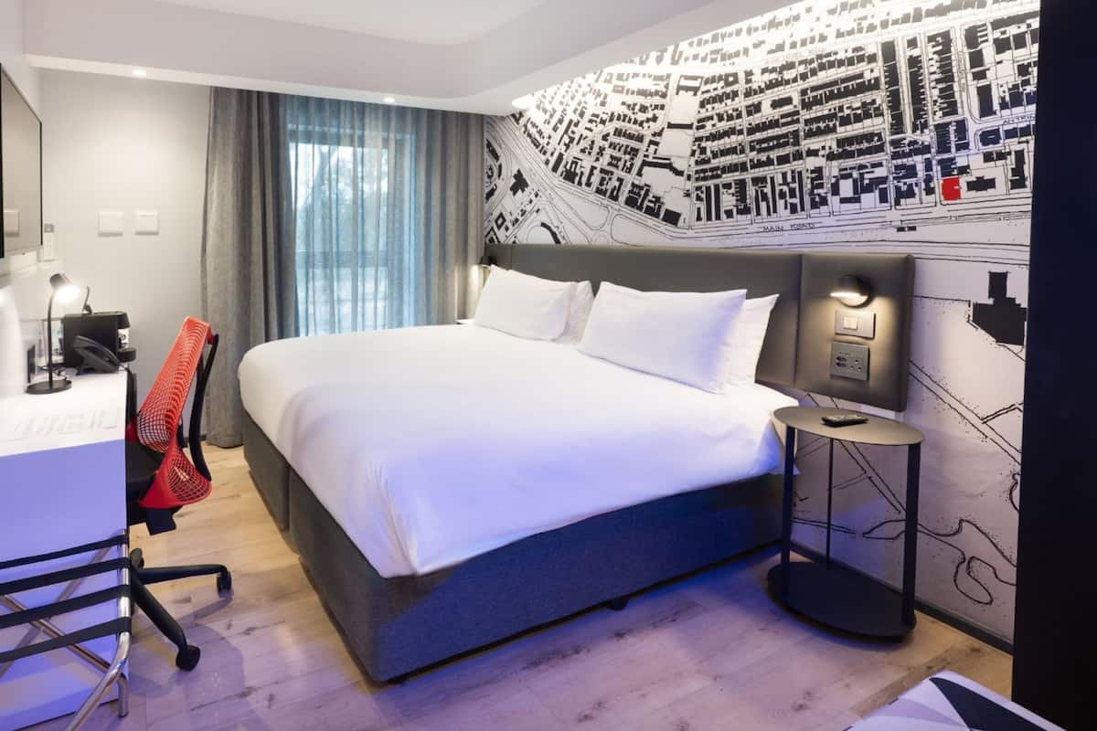 A modern hotel room with a large bed, a desk with a computer, and a wall-mounted TV.