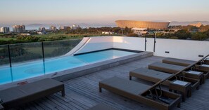 A rooftop pool with lounge chairs and a view of a stadium. - ANEW Hotel Green Point (Cape Town)
