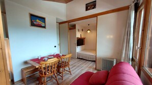 A cozy room with a wooden ceiling, a red sofa, a dining table with chairs, and a bed in the background.
