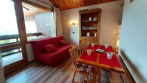 A cozy room with a red sofa, wooden dining table, and a shelf with dishes.