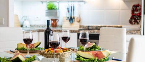 A modern kitchen with white cabinets, a glass dining table, and a bottle of wine.