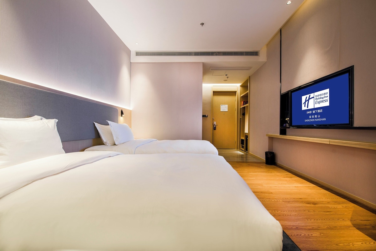 A hotel room with a large bed, a television on the wall, and a hallway leading to the bathroom.
