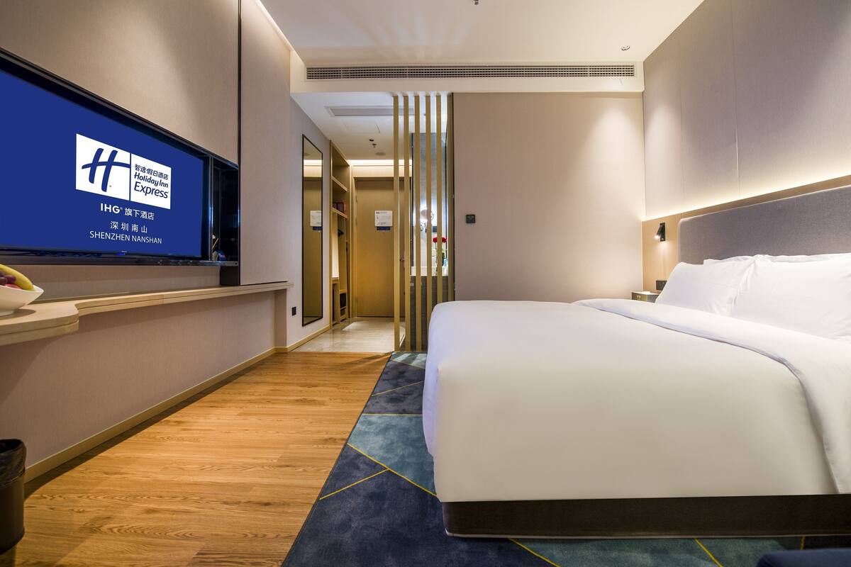A hotel room with a bed, a TV on the wall, and a wooden floor.