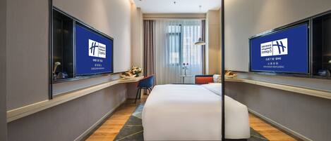A hotel room with a large bed, a desk with a computer, a chair, and a TV on the wall.