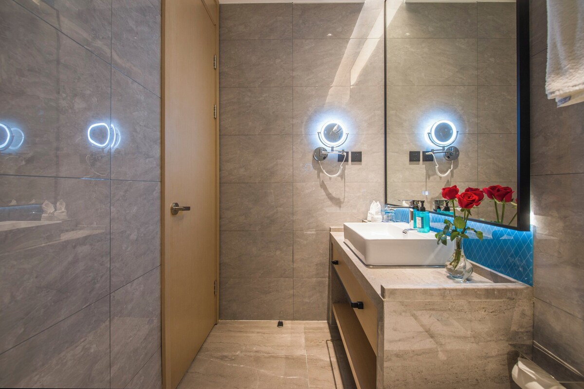 A modern bathroom with a marble floor, a white sink, and a mirror with built-in lighting.