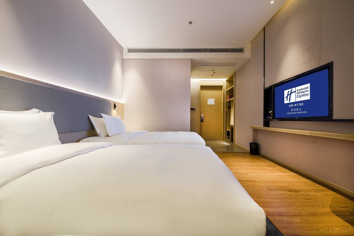 A hotel room with a large bed, a television mounted on the wall, and a wooden floor.