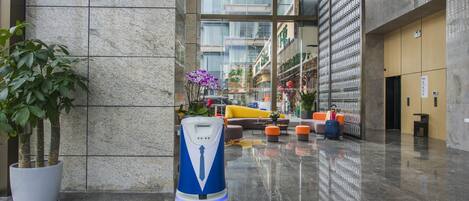 Eine moderne Lobby mit Marmorboden, einem Reinigungsroboter und einer Sitzecke mit orangefarbenen und gelben Stühlen.