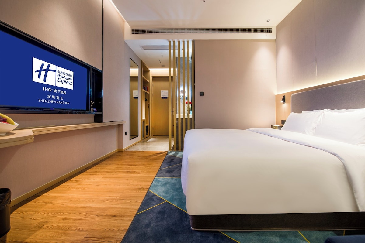 A hotel room with a bed, a TV on the wall, and a wooden floor.