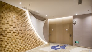 A modern hotel lobby with a wooden textured wall, a geometric patterned floor, and a large door with a light switch. - Holiday Inn Express Shenzhen Nanshan by IHG (Shenzhen)