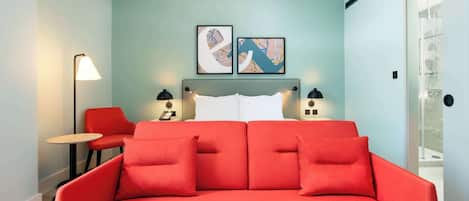 A modern room with a red sofa, a small table, and two chairs. There are two framed artworks on the wall above the sofa.