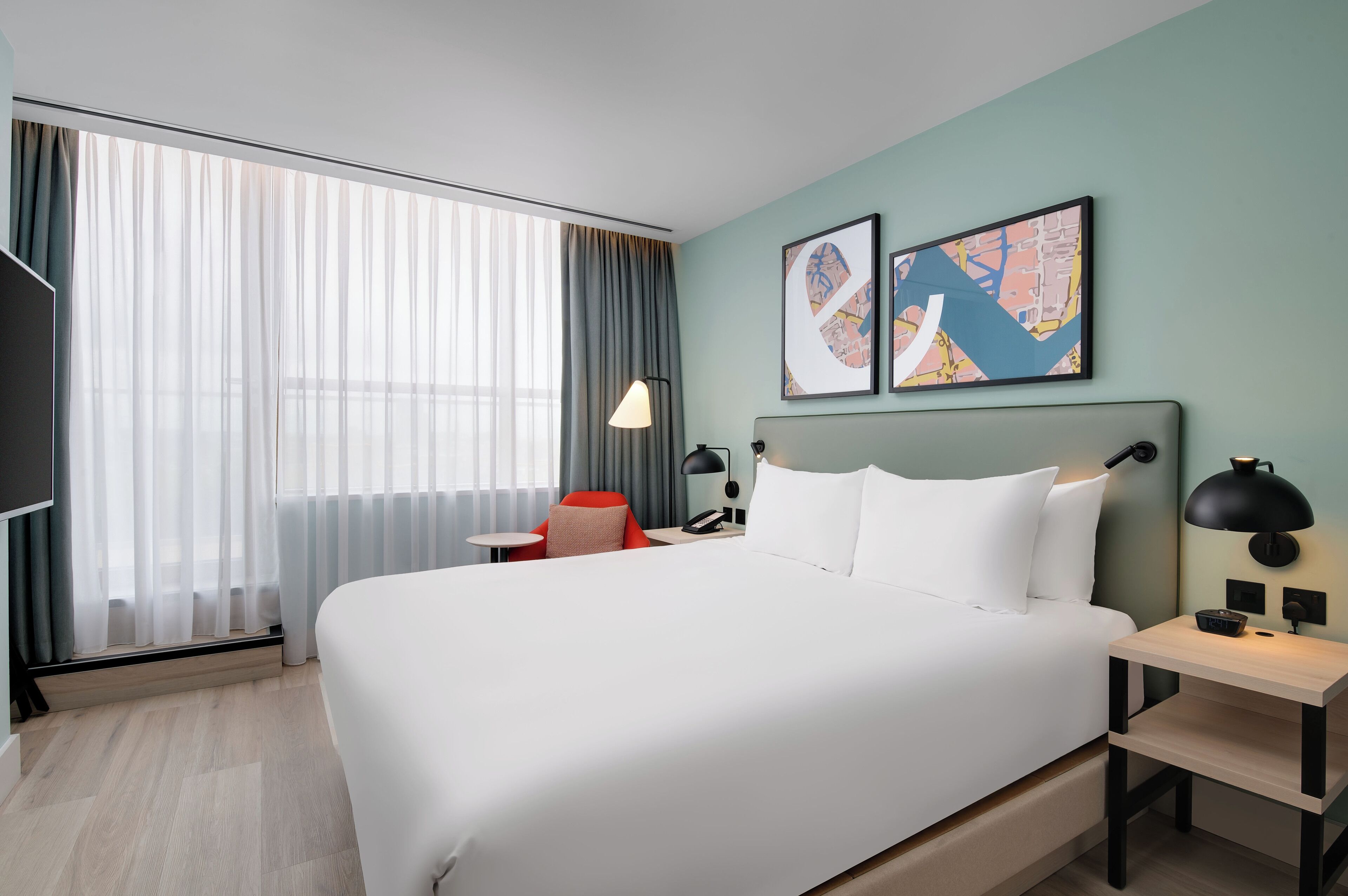 A modern hotel room with a large bed, a desk, a chair, and a TV.