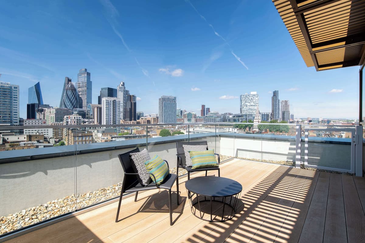 Une terrasse sur le toit, avec deux chaises et une table, d’où l’on peut admirer un panorama sur la ville, avec ses bâtiments modernes.