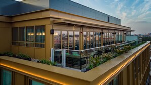 Un edificio moderno con amplios ventanales y una terraza en la azotea con asientos al aire libre.