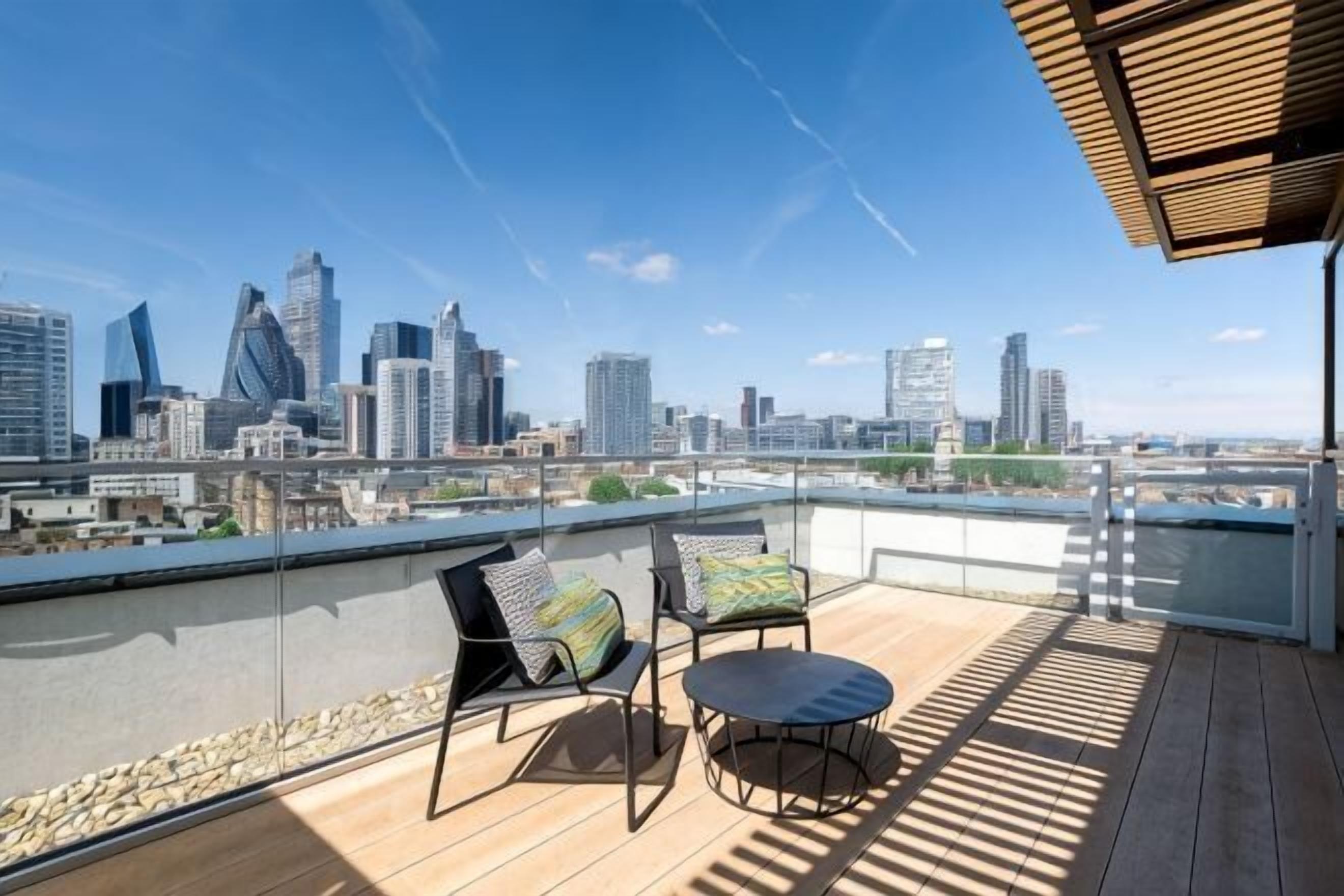 A rooftop terrace with a city skyline view, a wooden deck, and two chairs with cushions.
