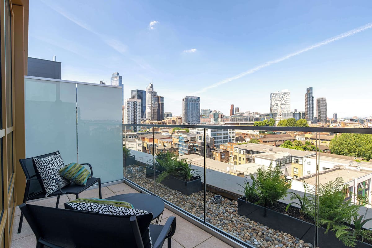 Un balcon avec vue sur la ville, une paroi en verre et des sièges d’extérieur.