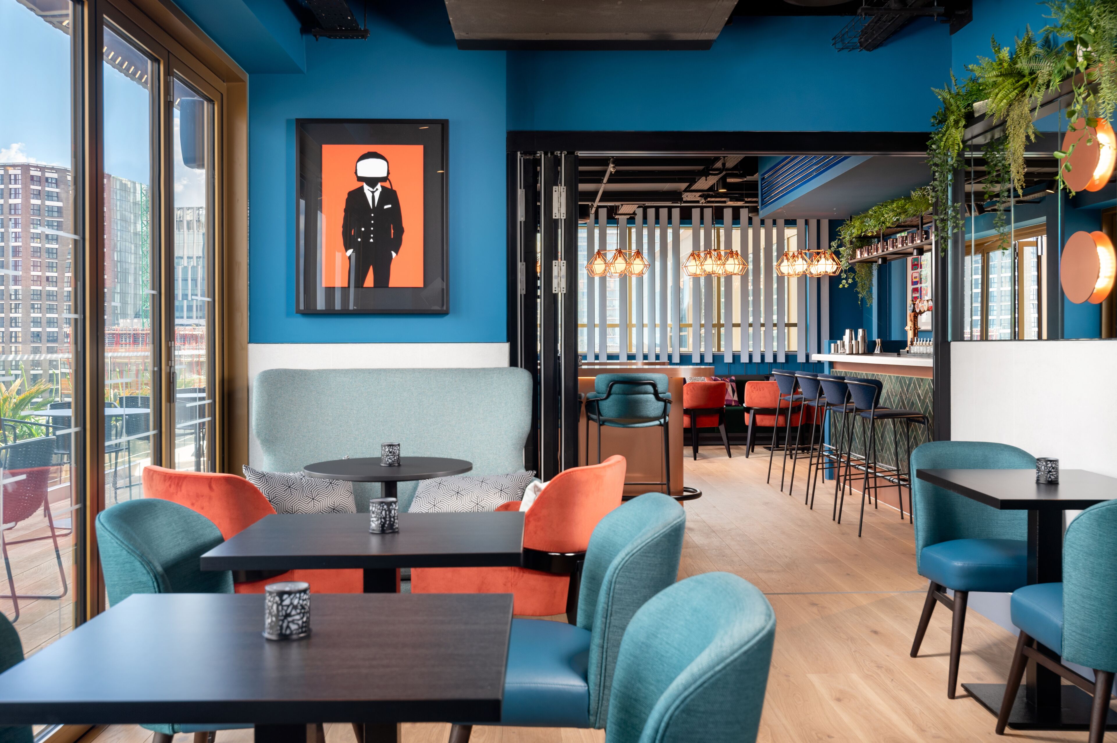 Un restaurante moderno con paredes azules, sillas coloridas y un amplio ventanal con vistas a la ciudad.