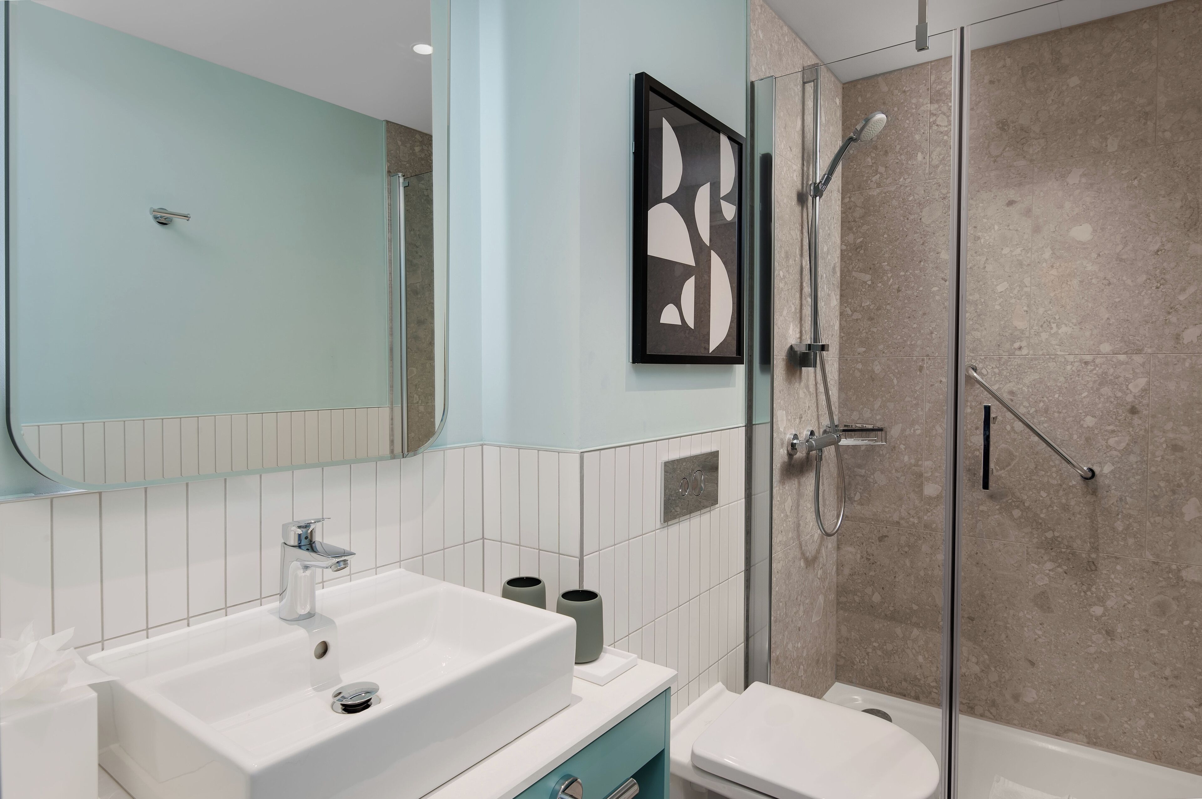 A modern bathroom with a large mirror, a white sink, a toilet, and a glass-enclosed shower area.