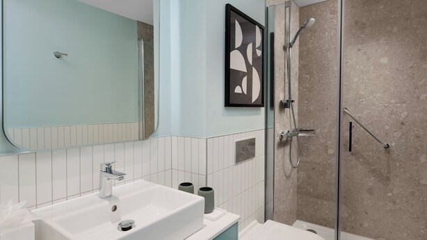 Une salle de bain moderne avec un grand miroir, un lavabo blanc, des toilettes et une douche séparée par une paroi de verre.