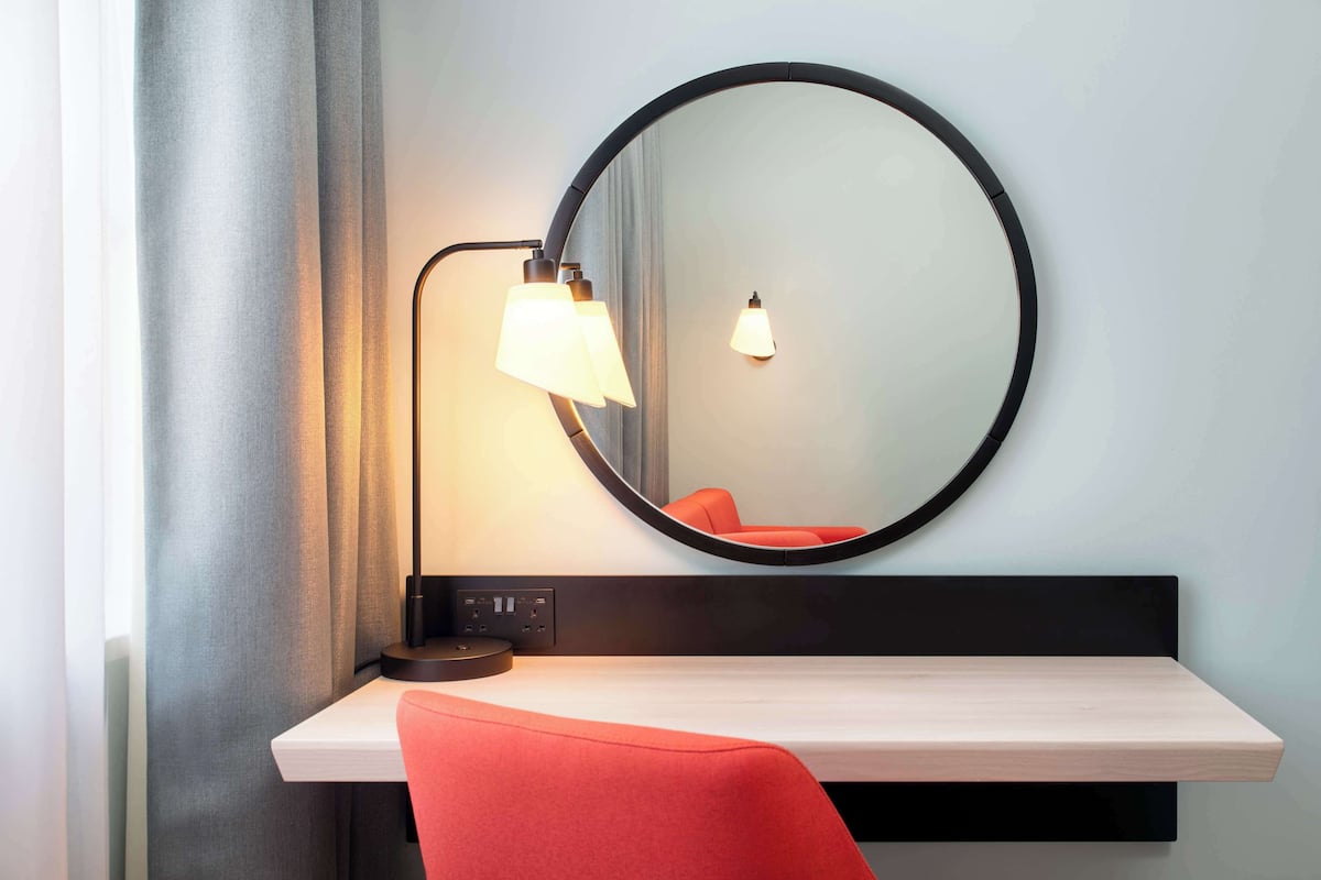 Une chambre moderne avec un miroir rond, un bureau et une chaise rouge.