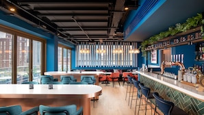Un área de bar moderna con mesas altas, taburetes y una barra equipada con utensilios.