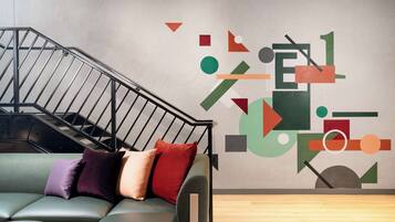 A modern interior with a staircase, a green sofa with cushions, and a geometric wall mural.