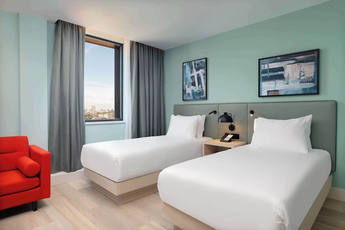 Une chambre d’hôtel avec deux lits, un fauteuil rouge et une vue sur la ville.