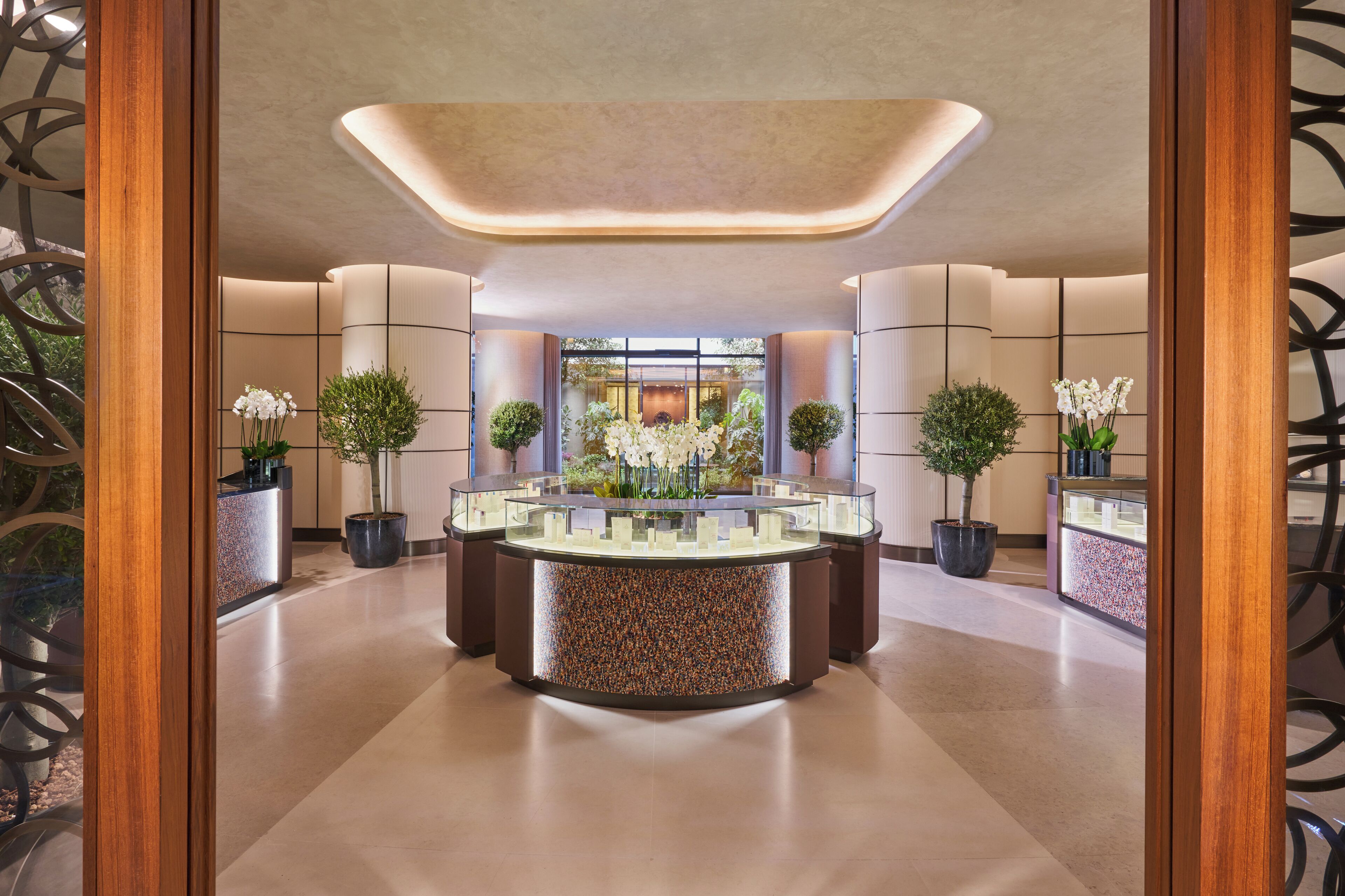 A modern lobby with a central round display table, potted plants, and a reception desk.