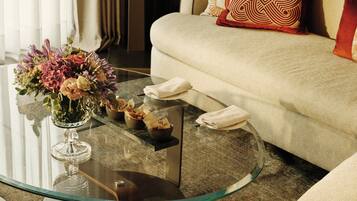 Una sala de estar moderna con una mesa de centro de vidrio, un centro de mesa floral y un sofá beige con cojines estampados.