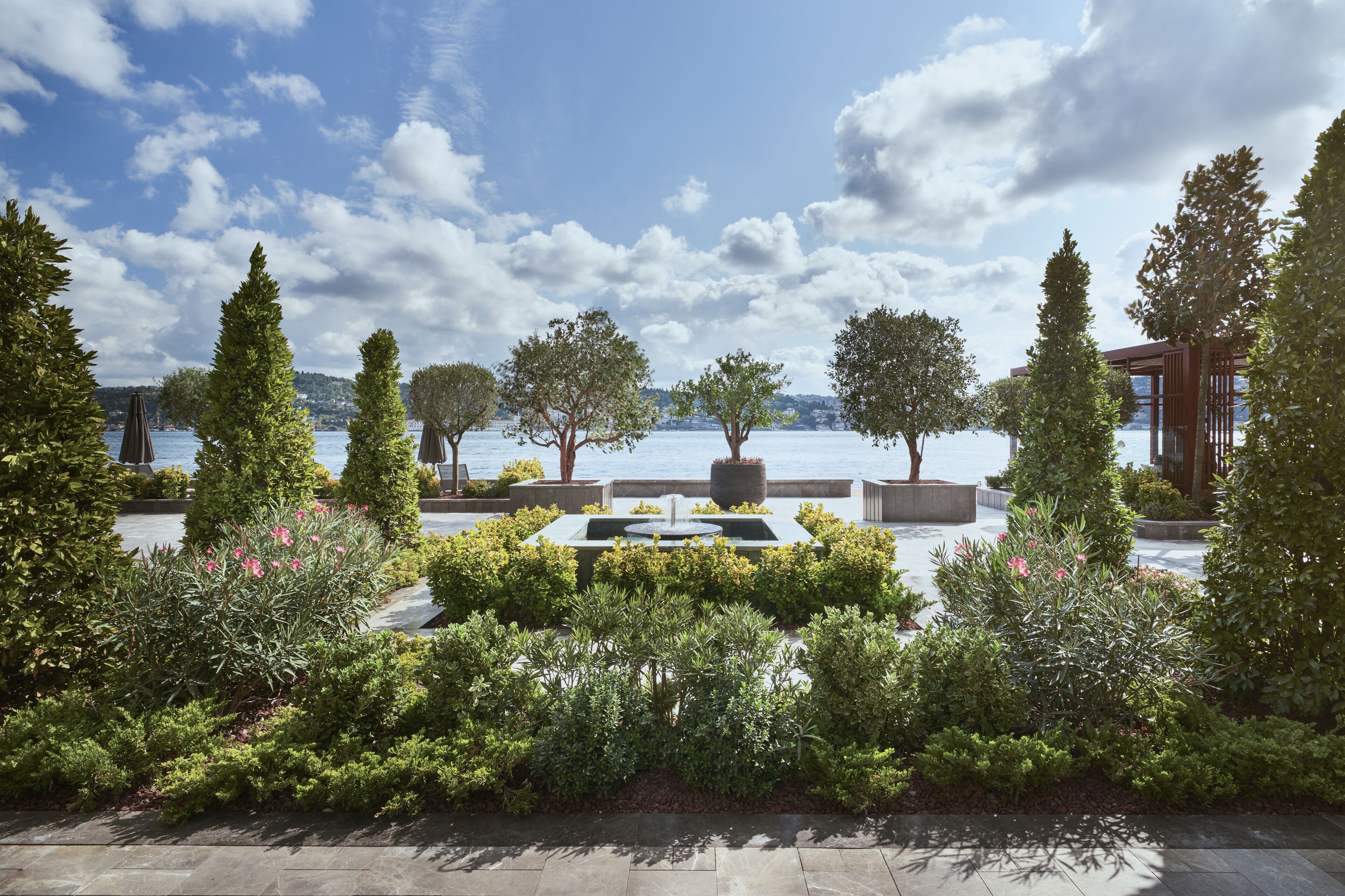 A landscaped garden with a water feature, trees, and a view of the water.