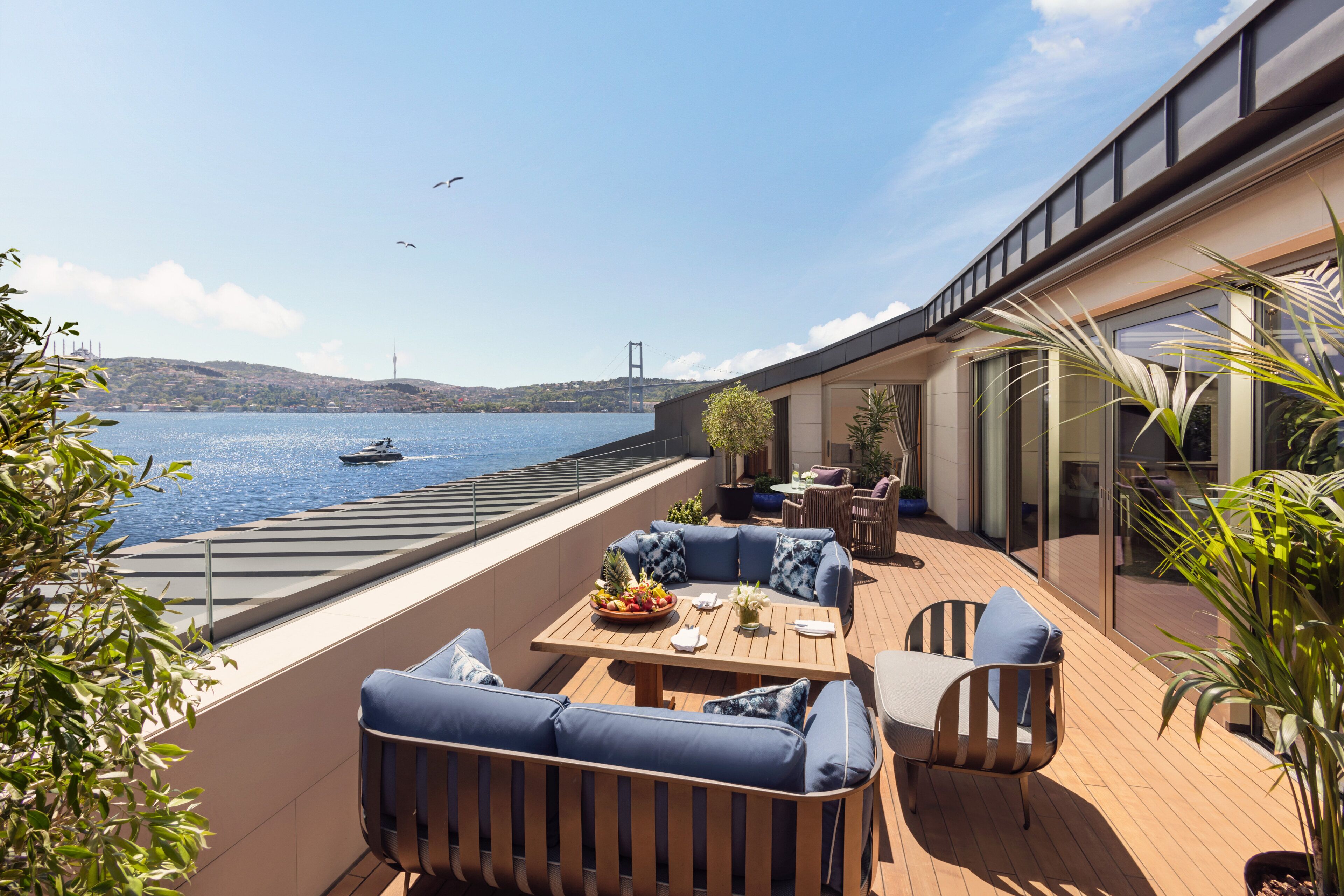 A modern outdoor seating area with a view of a body of water and a bridge in the distance.