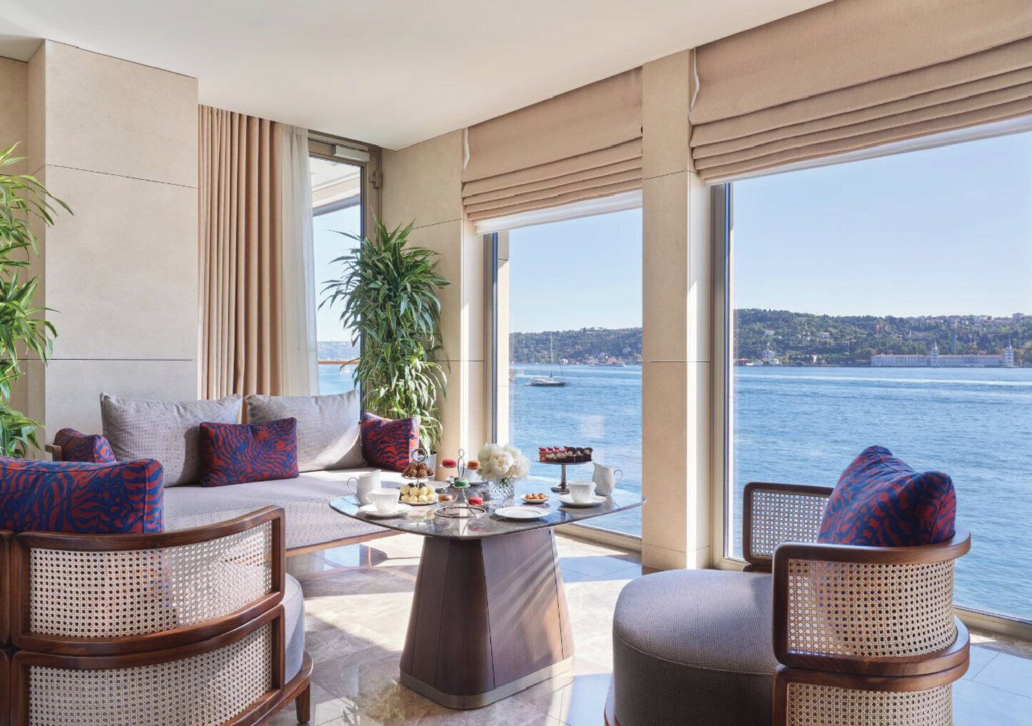 A modern living room with a large window overlooking a body of water, furnished with a sofa, chairs, and a coffee table.