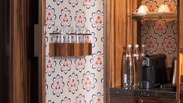 A kitchen with a patterned wallpaper, a coffee machine, and a glass display case with food items.