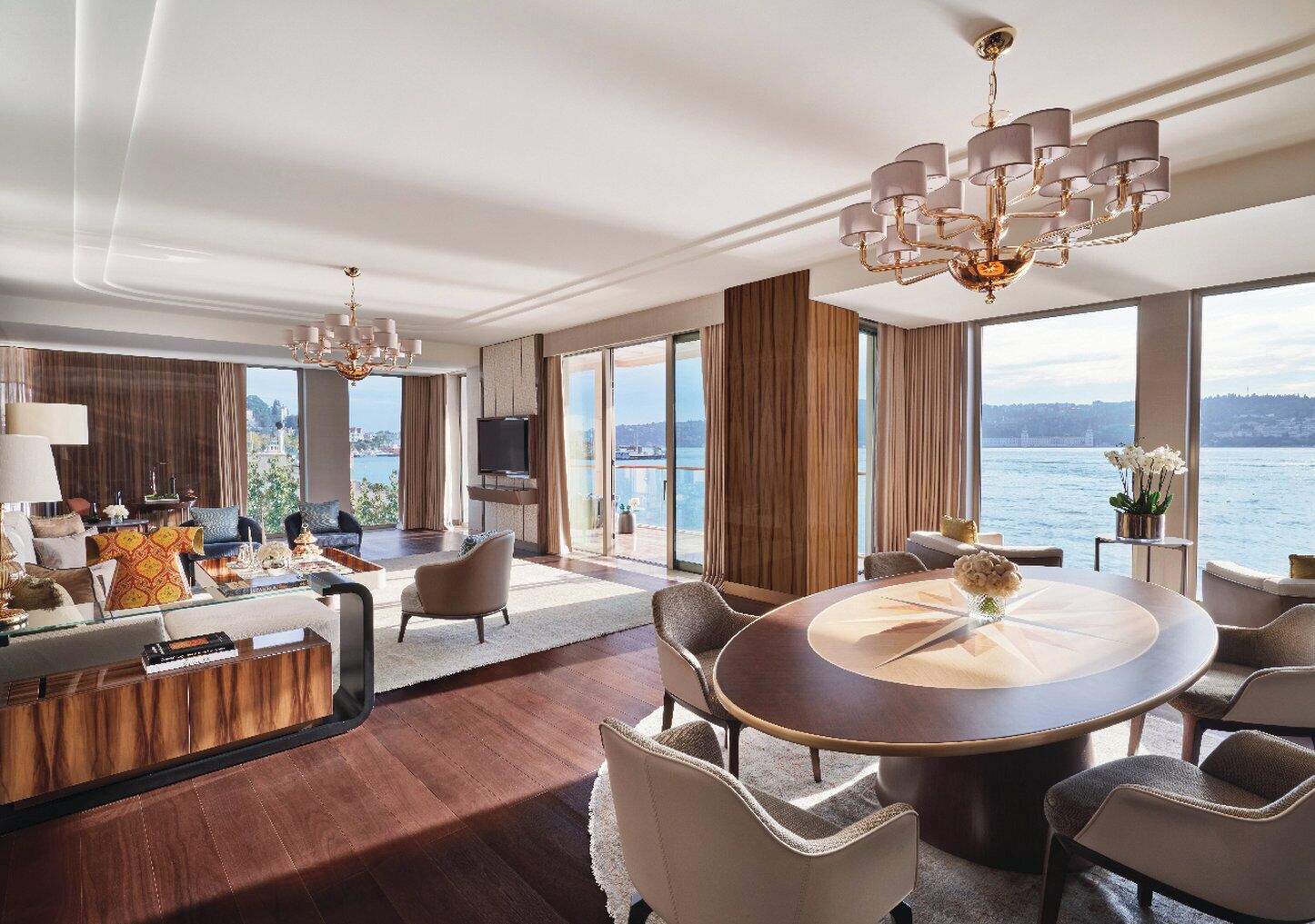 A spacious living room with a large round table, comfortable seating, and a view of the sea.