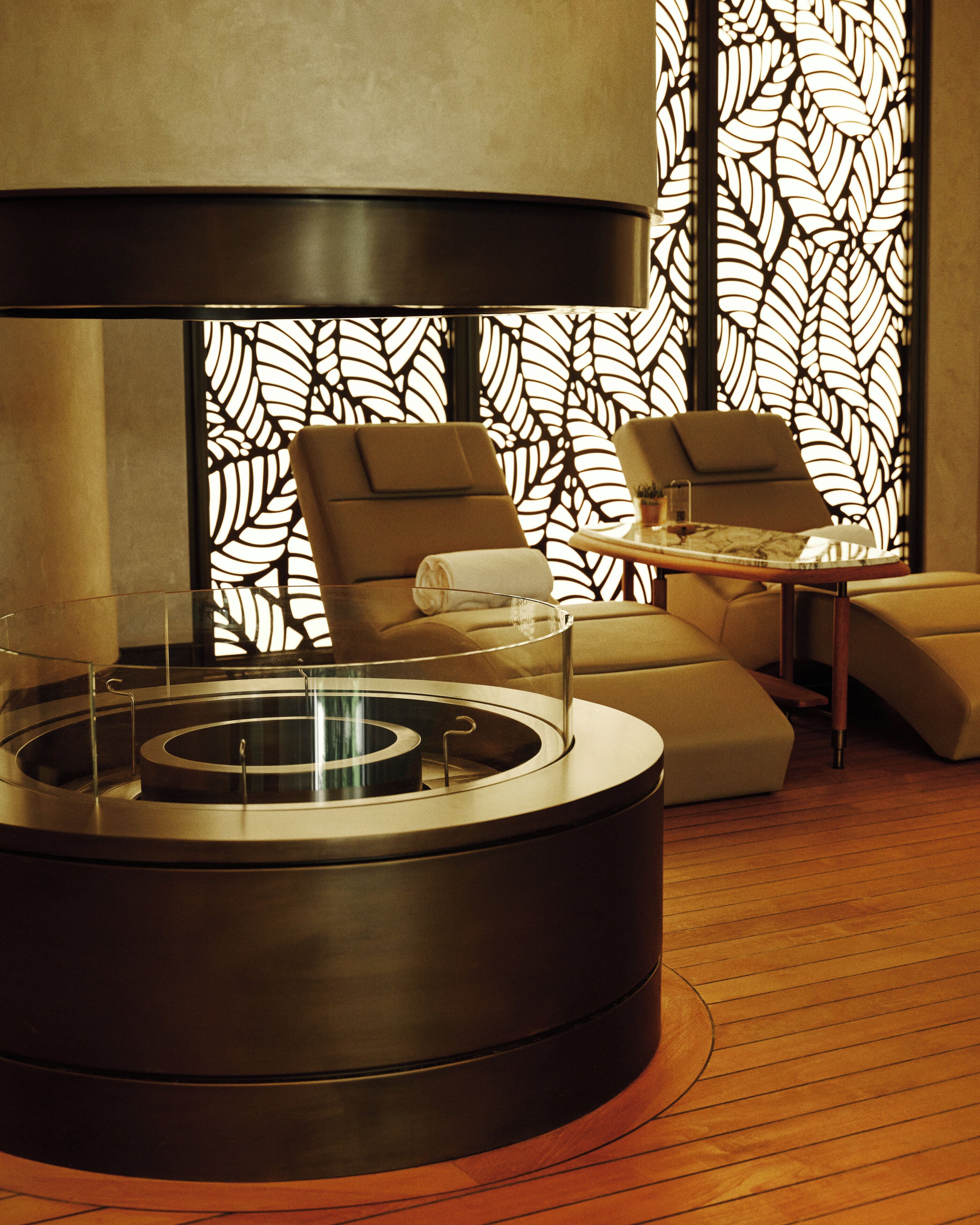 Un espace de détente moderne avec une table ronde centrale, deux canapés et un mur décoratif orné de motifs de feuilles.