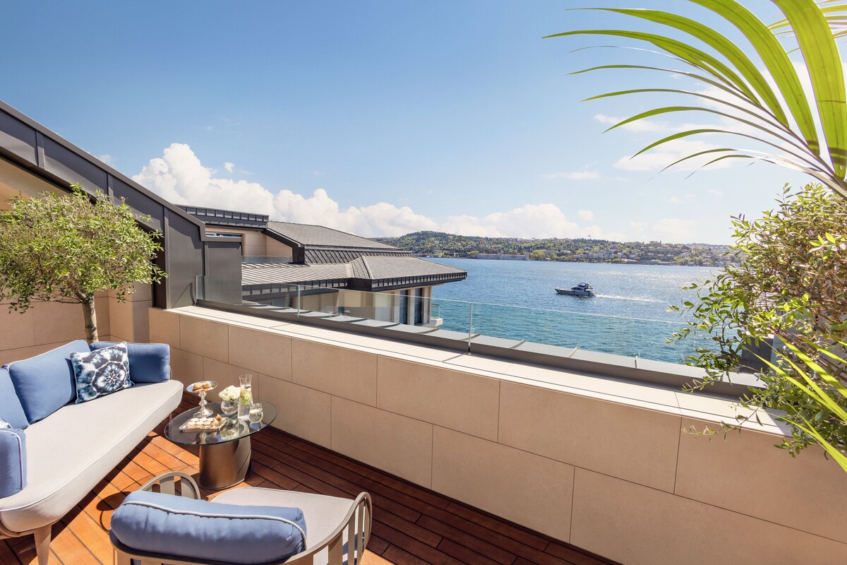 A balcony with a view of a lake, a dining table with chairs, and a sofa.
