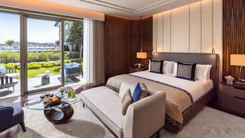 A hotel room with a large bed, a sitting area with a glass table, and a view of a landscaped garden.