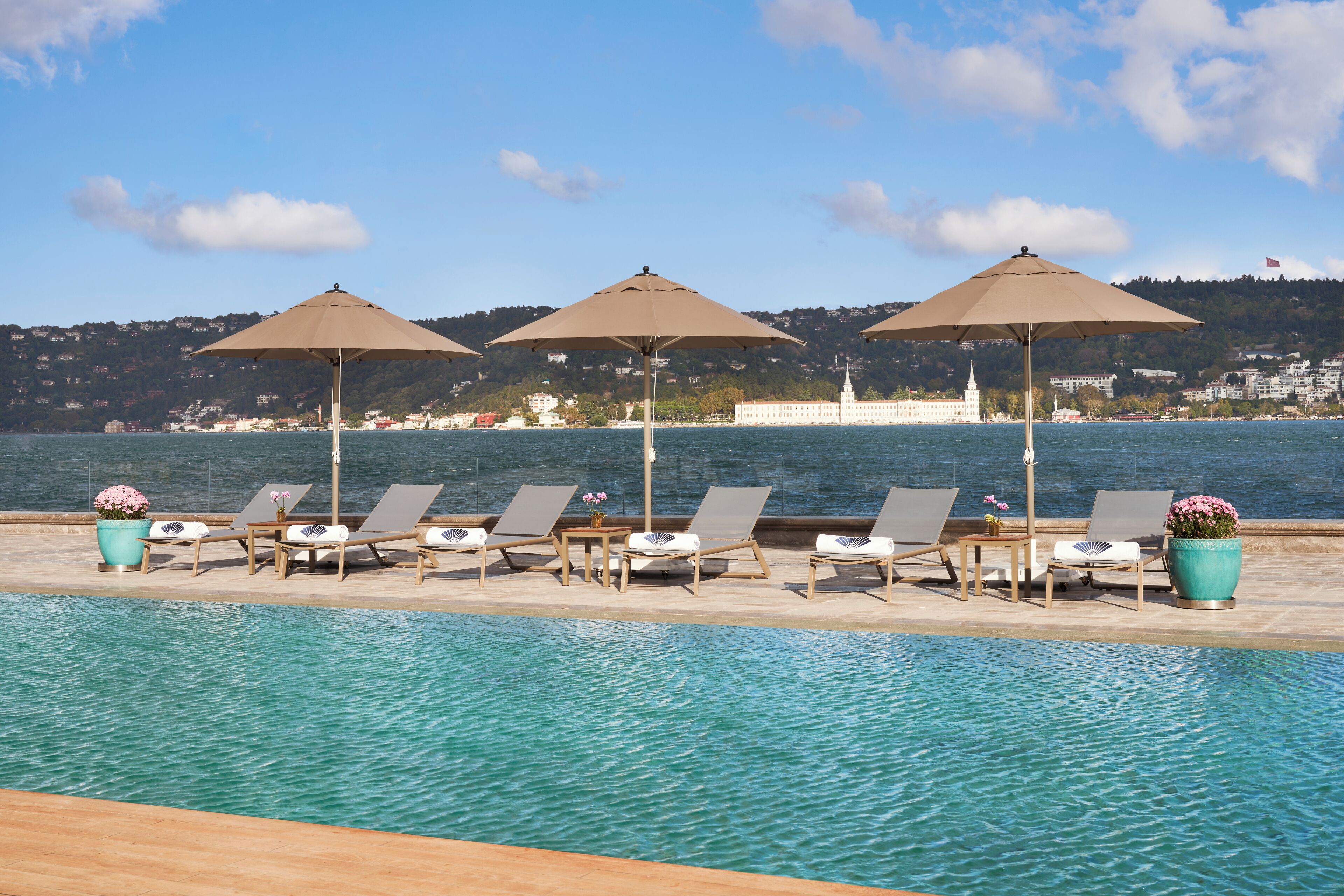 A poolside area with lounge chairs and umbrellas, overlooking a body of water with a distant building.