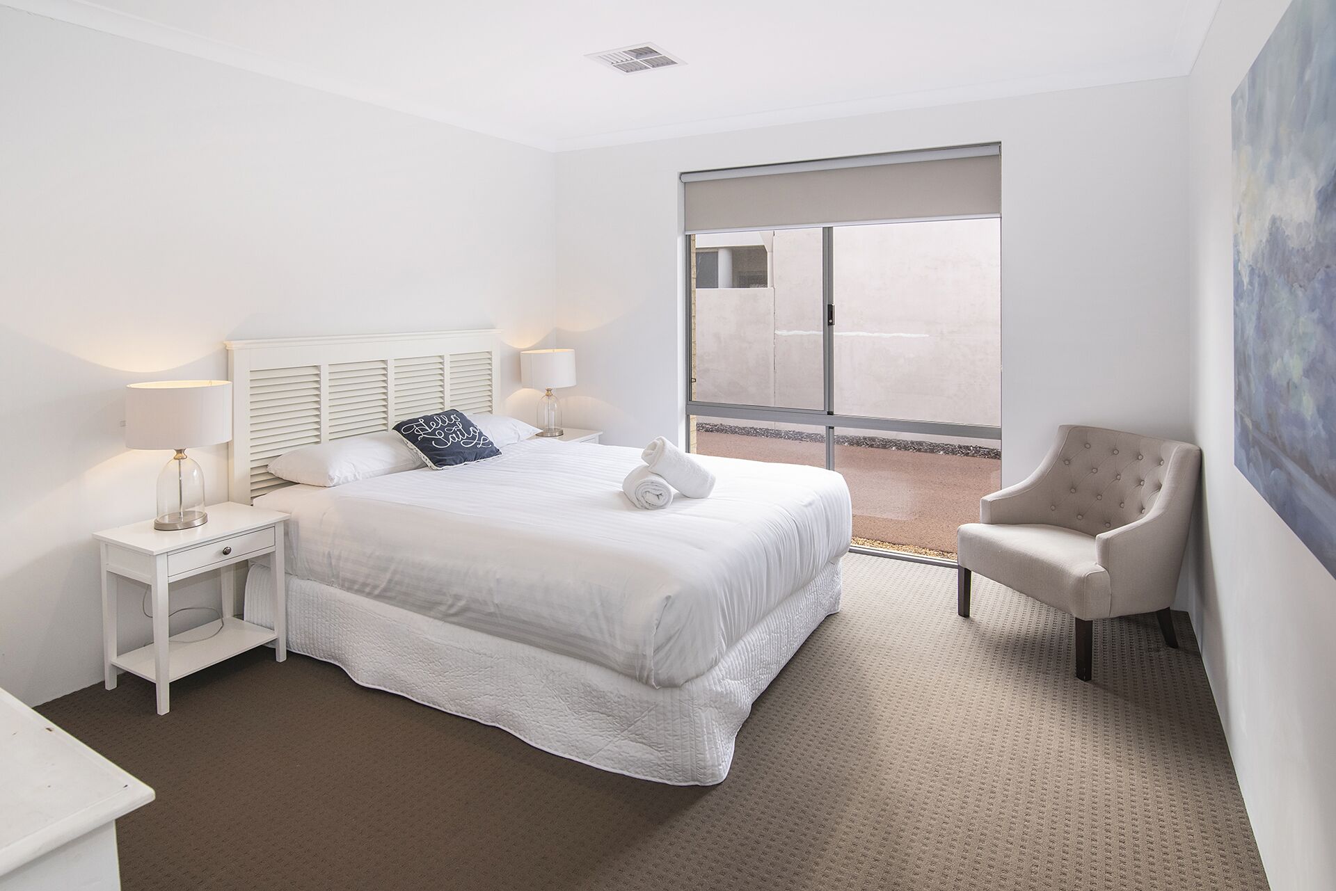 A hotel room with a large bed, two bedside tables, a chair, and a view of the outside.