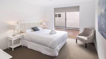 A hotel room with a large bed, two bedside tables, a chair, and a view of the outside.