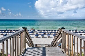 Une promenade en bois menant à une plage de sable blanc, parsemée de parasols bleus.