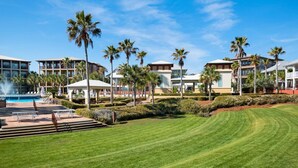 A resort with a swimming pool, palm trees, and well-maintained lawns.