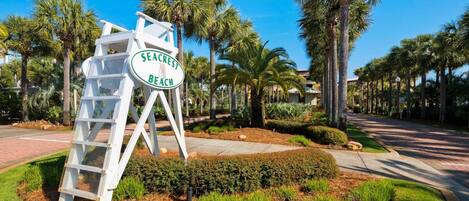 A sign for Seacrest Beach with a white structure and greenery around.
