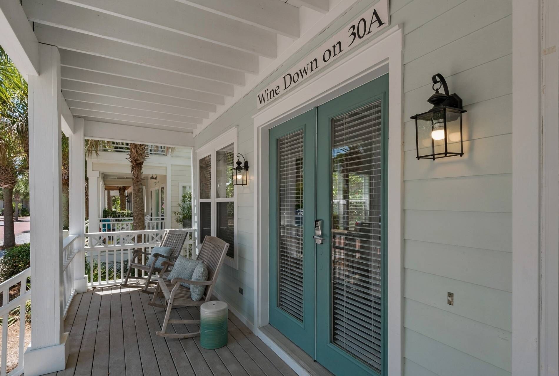 A porch with rocking chairs and a green door, labeled "Wine Down on 30A".