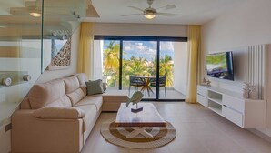 A modern living room with a sofa, coffee table, TV, and a view of palm trees through large windows. - Elegant and spacious Penthouse with View (Punta Cana)