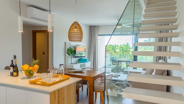 A modern kitchen with a wooden island, a dining area with a glass table, and a staircase with white railings. - Elegant and spacious Penthouse with View (Punta Cana)