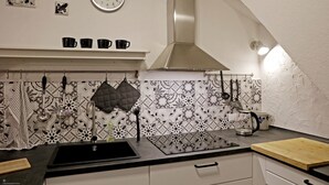 A kitchen with a black sink, a stove, a clock, and a hanging pot rack. - Gemütliches Stadthaus im Herzen der Altstadt (Bad Dürkheim)