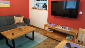 A living room with a sofa, coffee table, TV, and a small wooden table with books and a remote control. - Gemütliches Stadthaus im Herzen der Altstadt (Bad Dürkheim)