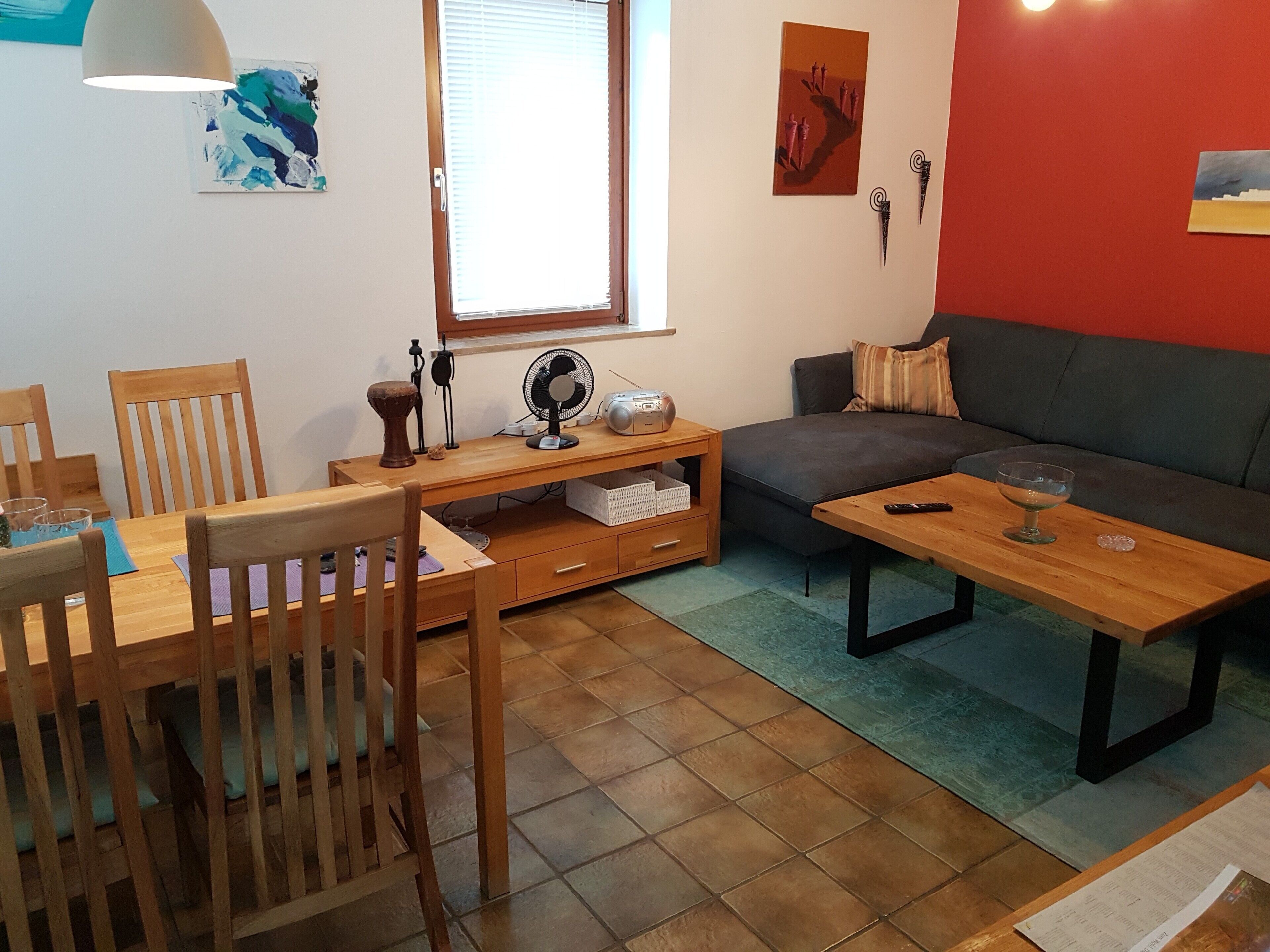A living room with a sofa, a dining table with chairs, a wooden coffee table, a floor lamp, and artwork on the walls.