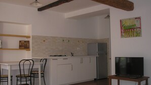 A compact kitchen with white cabinets, a built-in stove, and a refrigerator. There is a dining table with chairs and a television on a wooden stand. - GREEN RELAX II THE GREEN OF THE HILL (Torino)