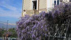 A two-story building with a balcony, a stone wall with purple flowers, and a clear sky. - GREEN RELAX II THE GREEN OF THE HILL (Torino)